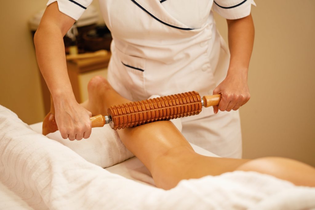 unrecognizable therapist performing maderotherapy on woman s legs during massage treatment at the spa min